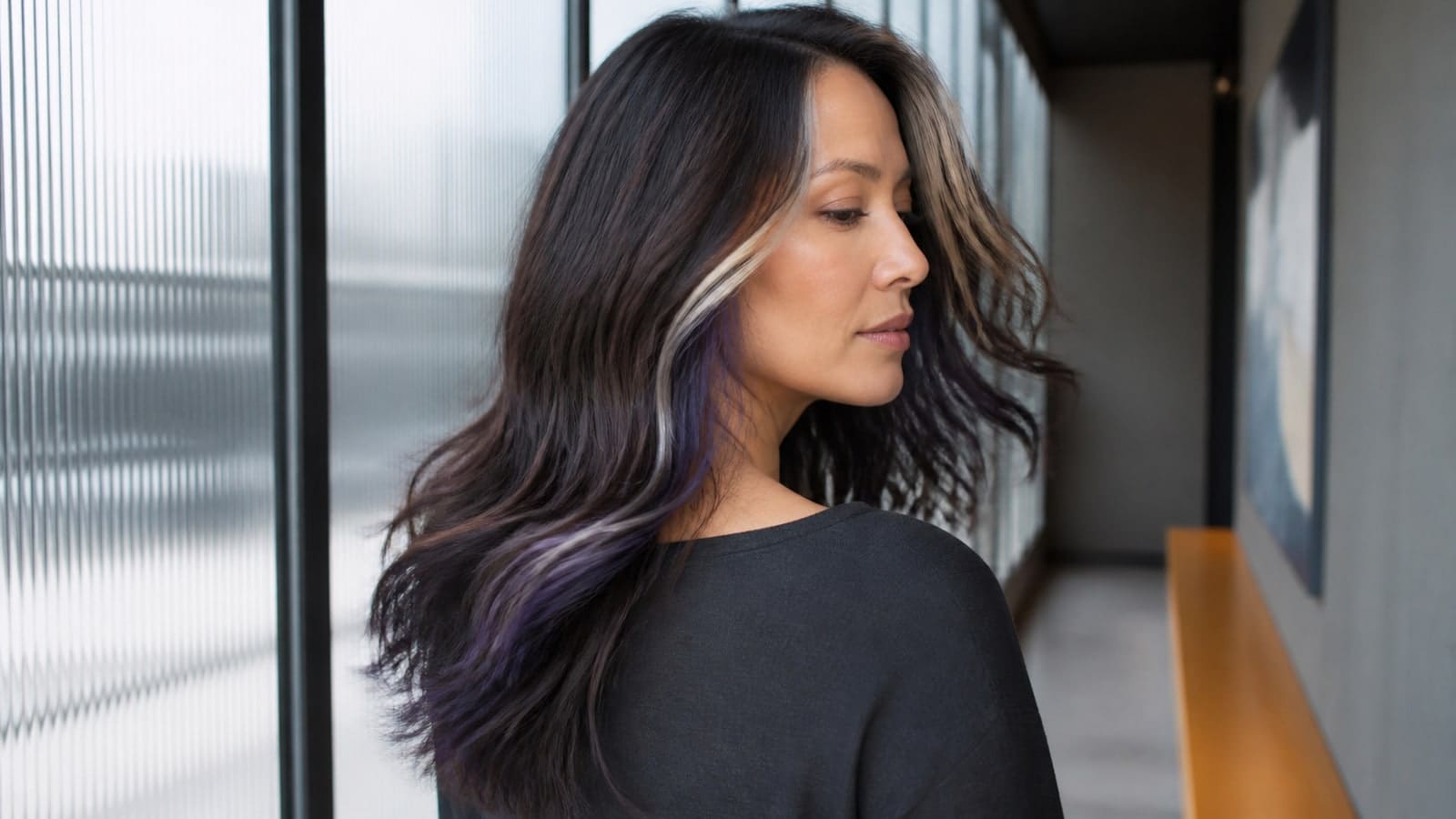 Woman turning beside a ribbed-glass window with glossy cool espresso waves, narrow icy face-framing ribbons, and a blue-violet underlayer