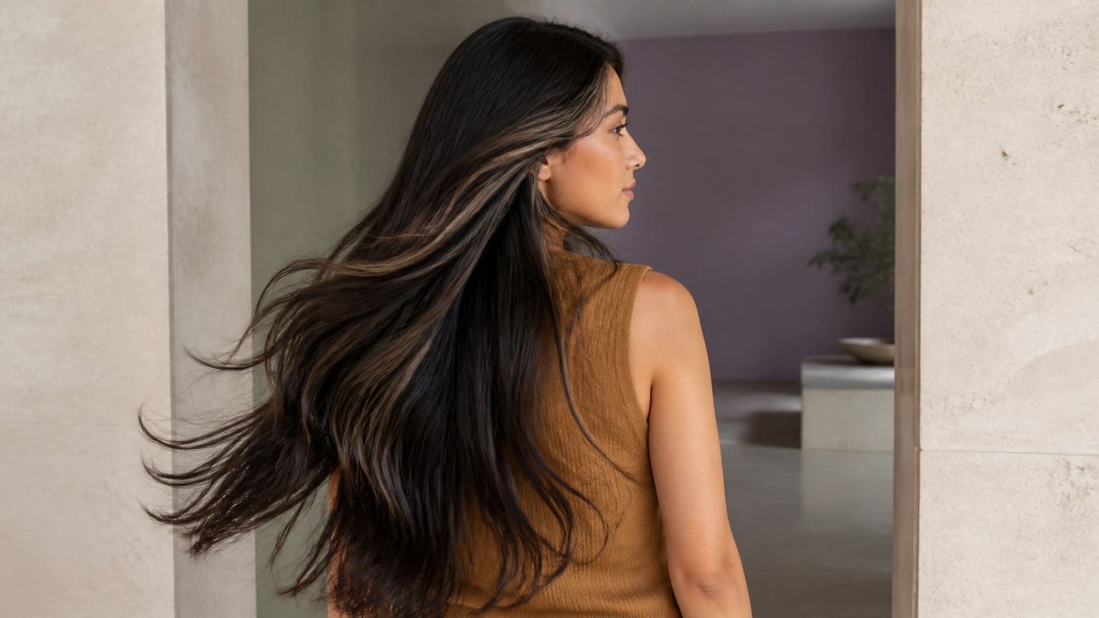 Woman turning through a doorway with narrow beige-brown ribbons near the part, wider lighter face-framing pieces, and a dominant near-black base