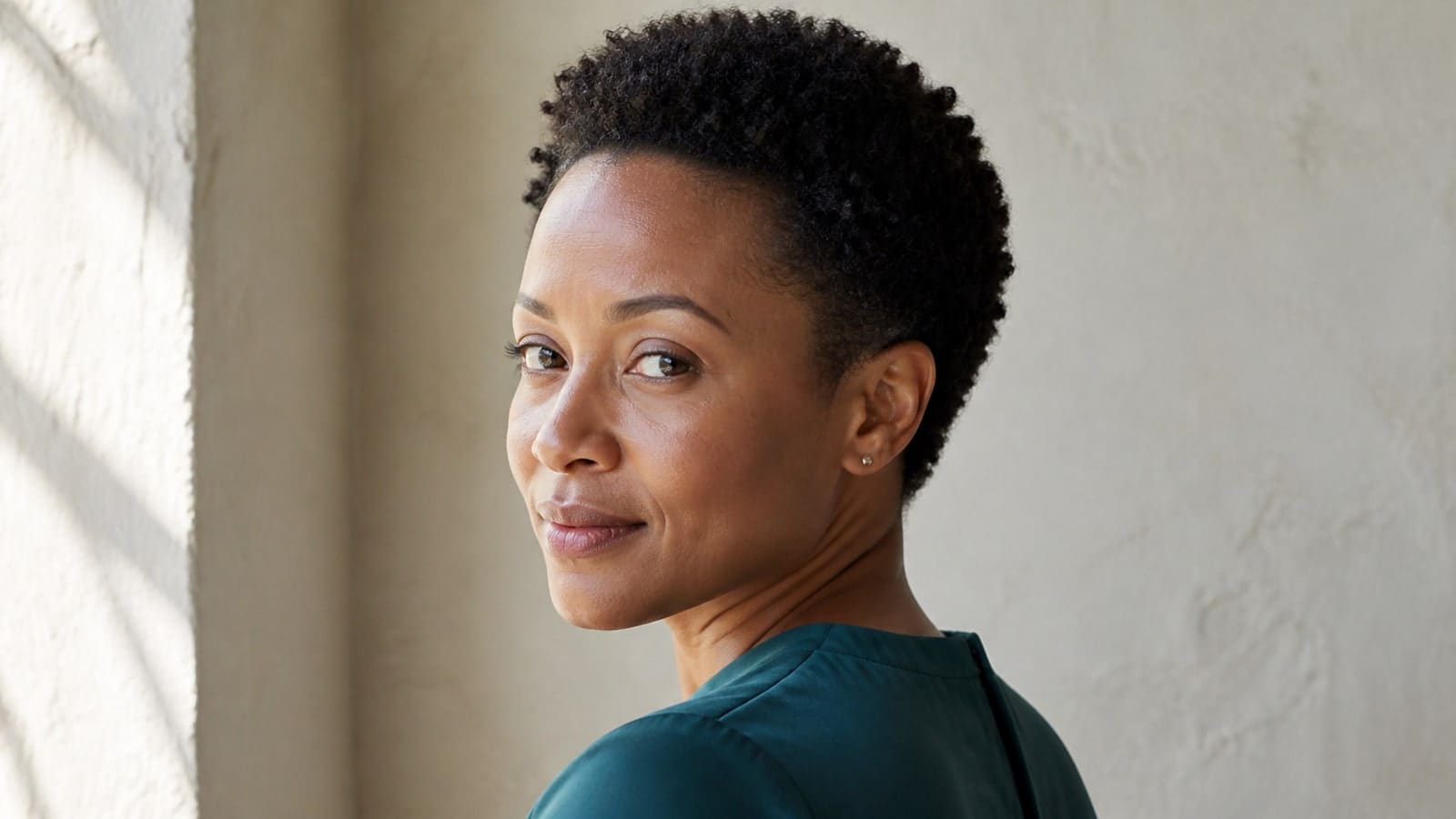 Oval-like face with an open forehead, dense coily ear-level crop, compact sides, and softly tapered nape